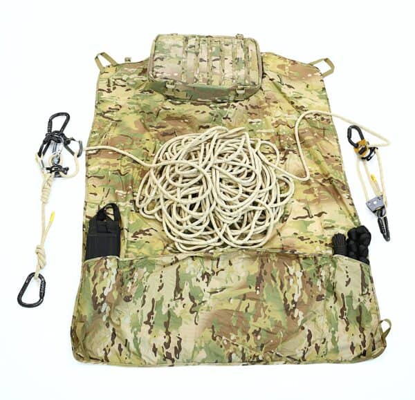 A camouflage mat displaying tactical rescue training gear, like a coiled rope, carabiners, and pouches, is laid out on a white background.