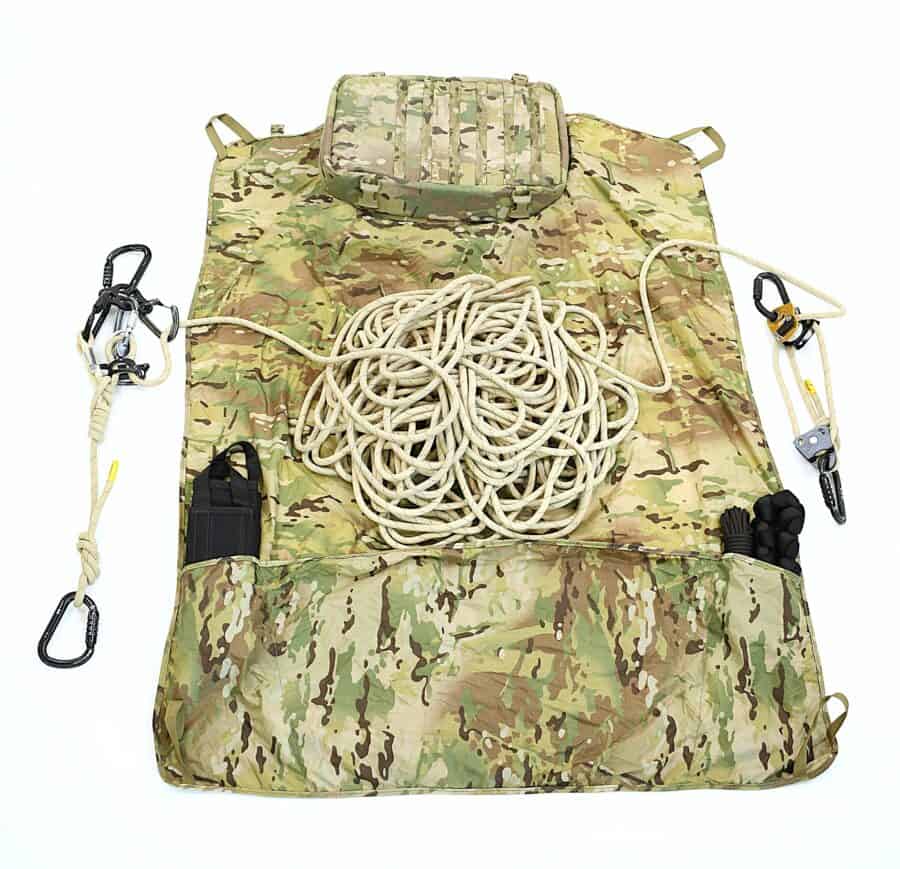 A camouflage mat displaying tactical rescue training gear, like a coiled rope, carabiners, and pouches, is laid out on a white background.