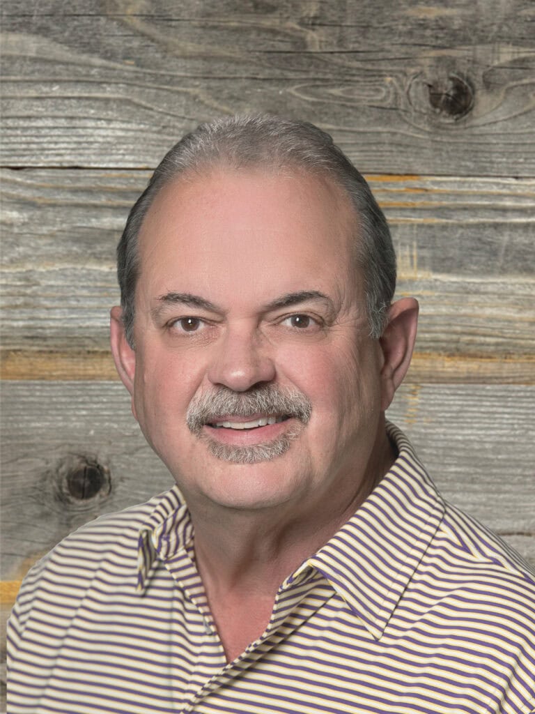 A person with short hair and a mustache is wearing a striped shirt, posing in front of a wooden backdrop, exuding the confidence of a fire rescue expert.