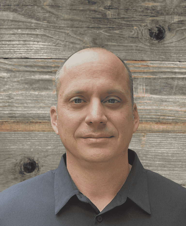 A man poses in front of a wooden plank background. The man is Rob Seei, Director of Tactical Rescue & Recovery at TribalCo Rescue.